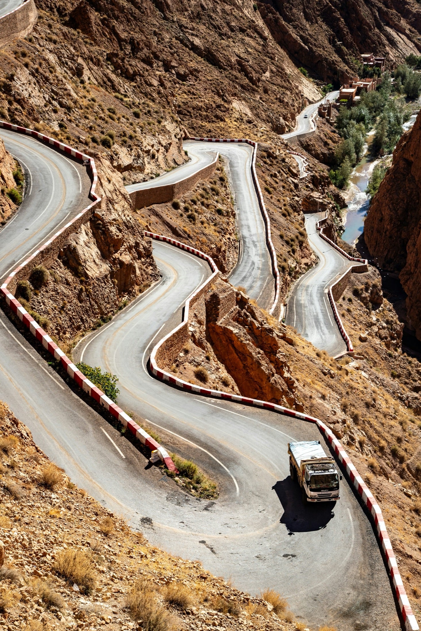 A truck climbing a tight switchback mountain pass, red-and-white barriers on the bends.